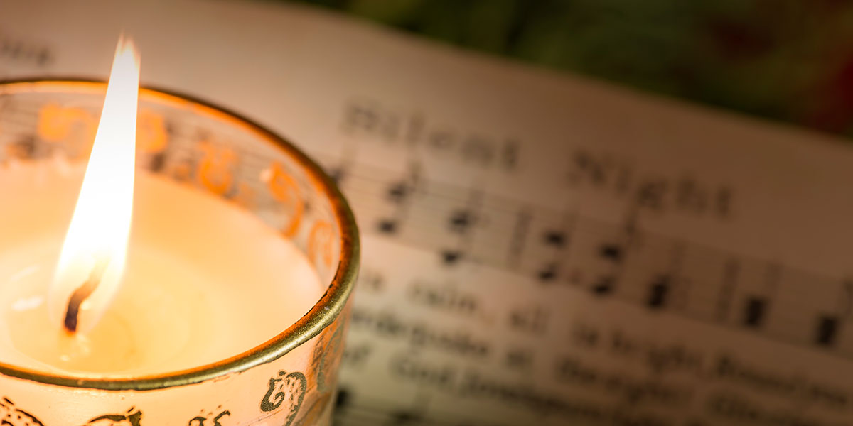 A lit candle in front of sheet music for Silent Night.