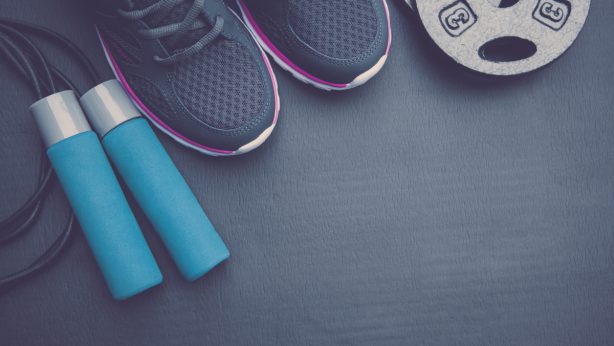 A pair of sneakers, a jump rope, a weight on a dark-colored floor.