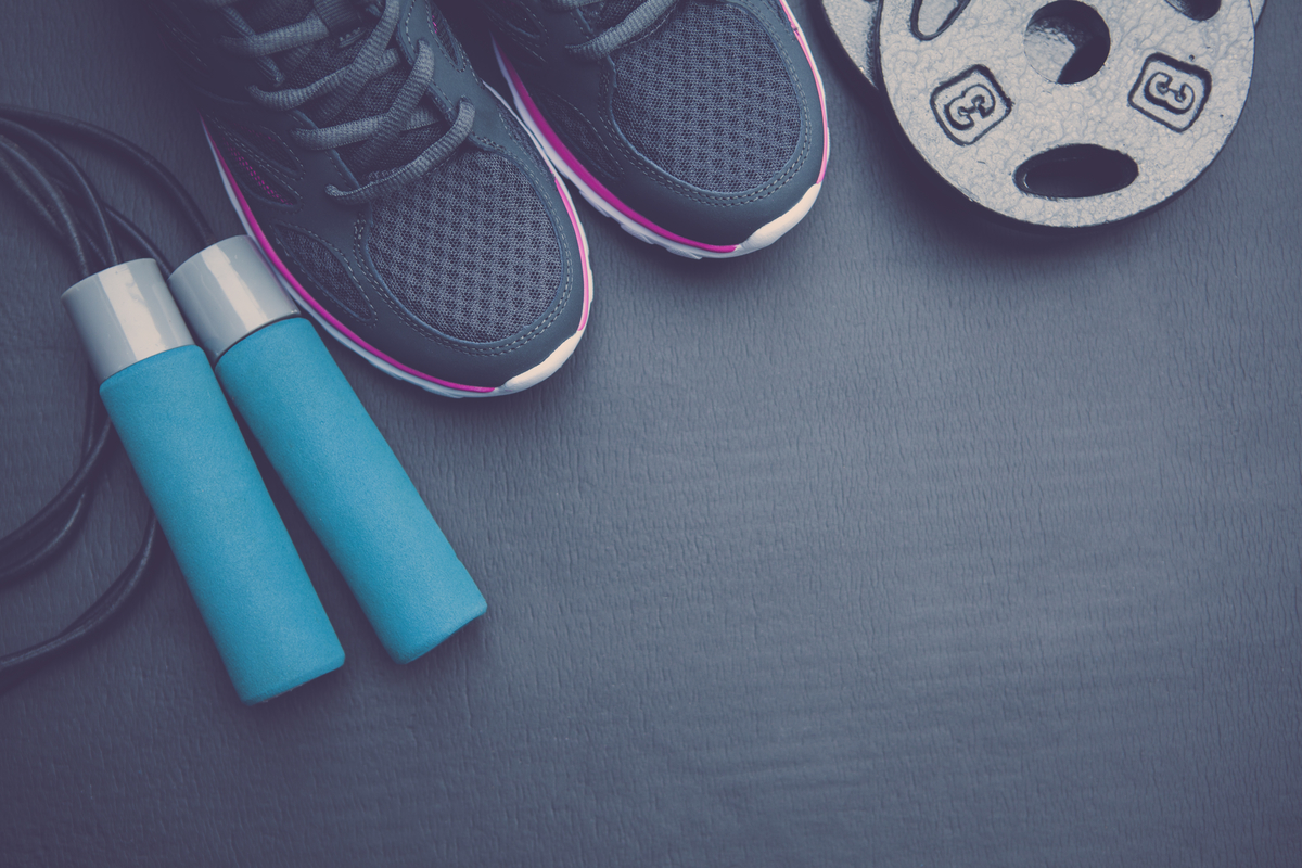 A pair of sneakers, a jump rope, a weight on a dark-colored floor.