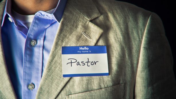 A nametag that says "Hello, my name is Pastor" on the chest of a man wearing a button-down shirt and jacket.