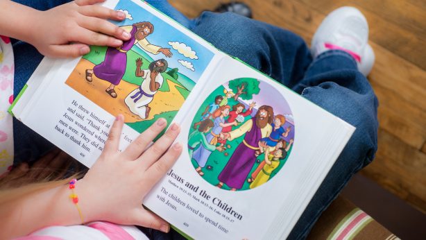 A children's book about Jesus being held open by the hands of two children.