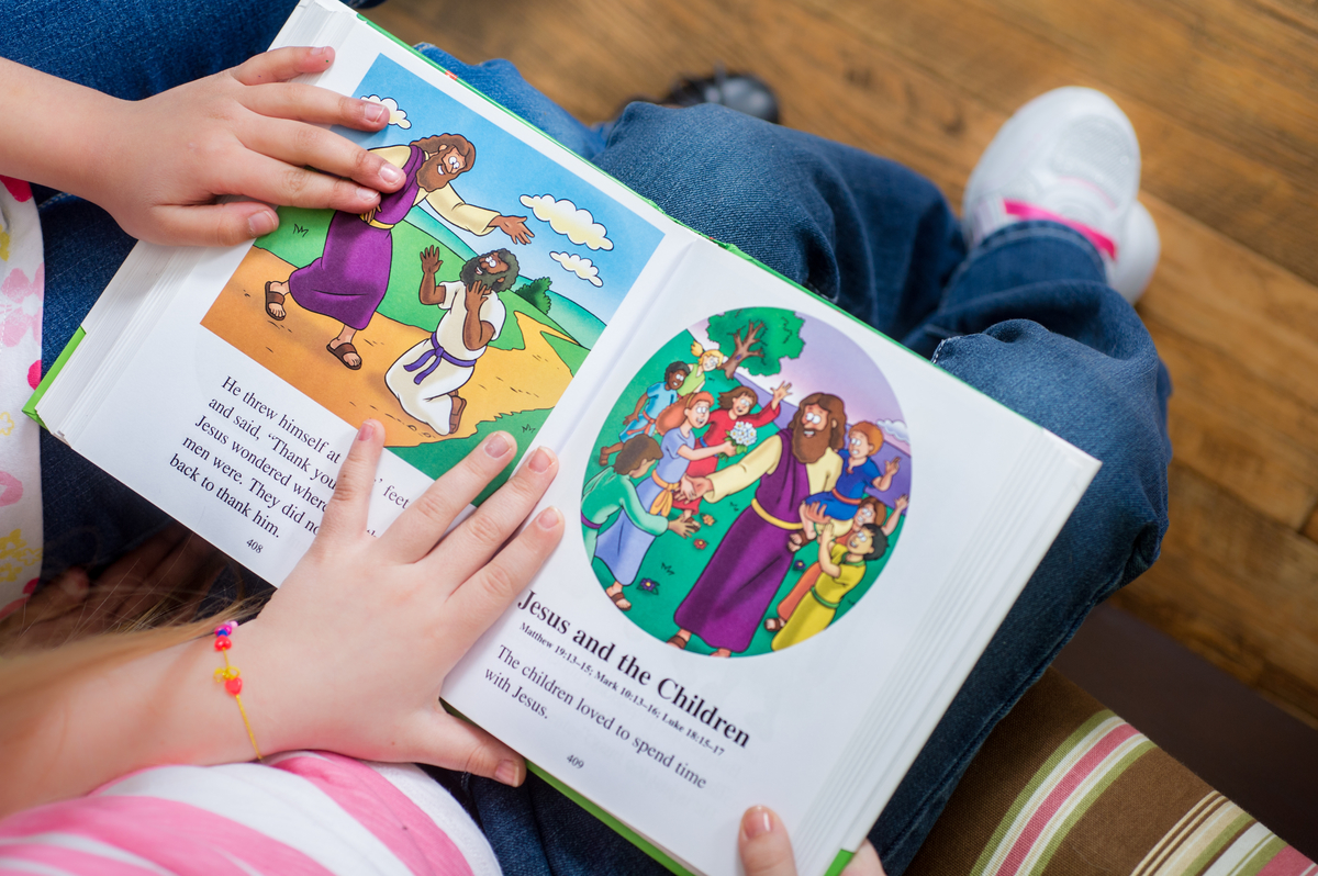 A children's book about Jesus being held open by the hands of two children.